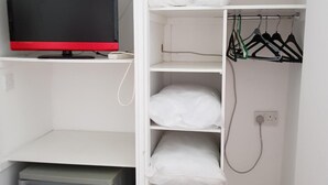 A white closet with shelves, a red and black television, a small refrigerator, and a power outlet. - Chelford Guesthouse (Knutsford)