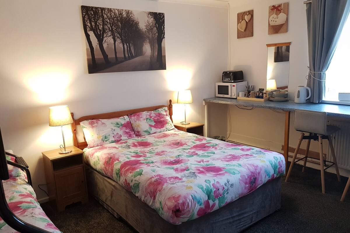 A bedroom with a bed, bedside lamps, a desk with a computer, a microwave, and a mirror.