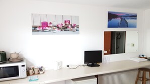 A kitchen with a microwave, toaster, and sink. There are decorative items on the counter and a large window with a view of a lake and a dock. - Chelford Guesthouse (Knutsford)