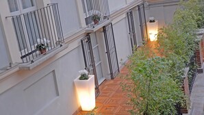 Un estrecho pasillo con suelo de baldosas, barandillas de metal y plantas en macetas.