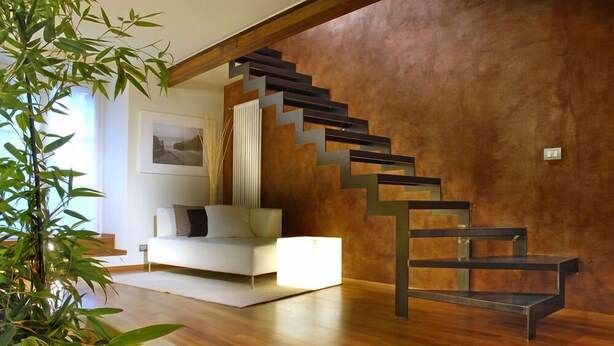 Una sala de estar moderna con una escalera de madera, un sofá blanco y una planta grande en maceta.