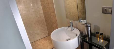 Un baño moderno con un lavabo blanco, un tocador de vidrio, un espejo y una zona de ducha.