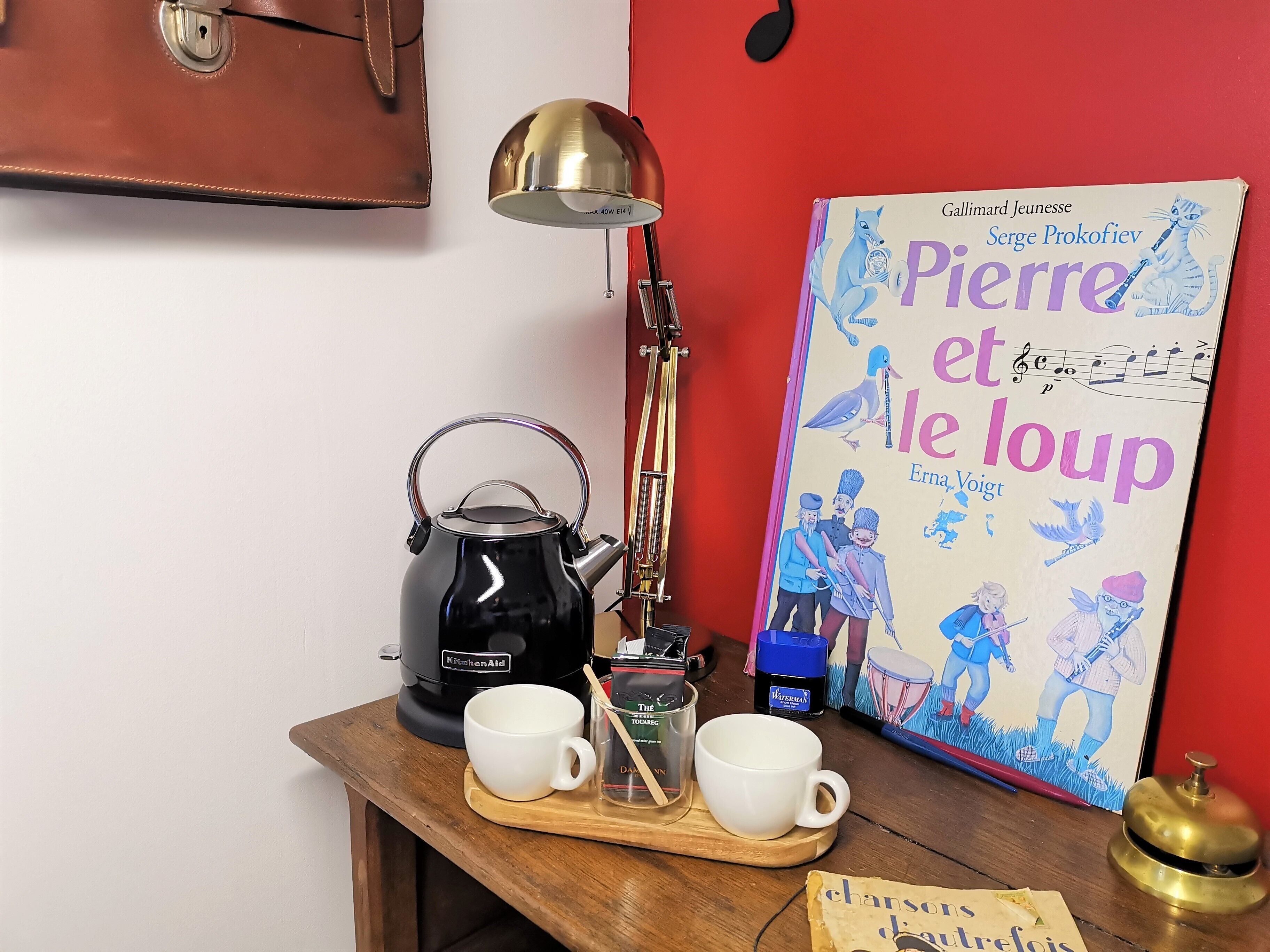 Un comptoir de cuisine avec une bouilloire, deux tasses, un plateau, un livre et une lampe.