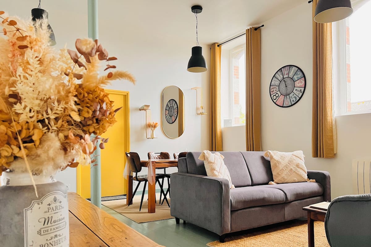 A living room with a grey sofa, wooden coffee table, and a vase with dried flowers.
