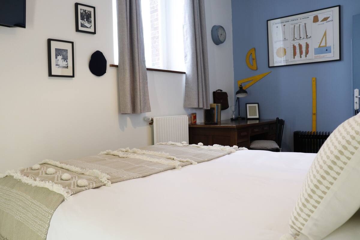A bedroom with a bed, a desk, a chair, and a radiator.