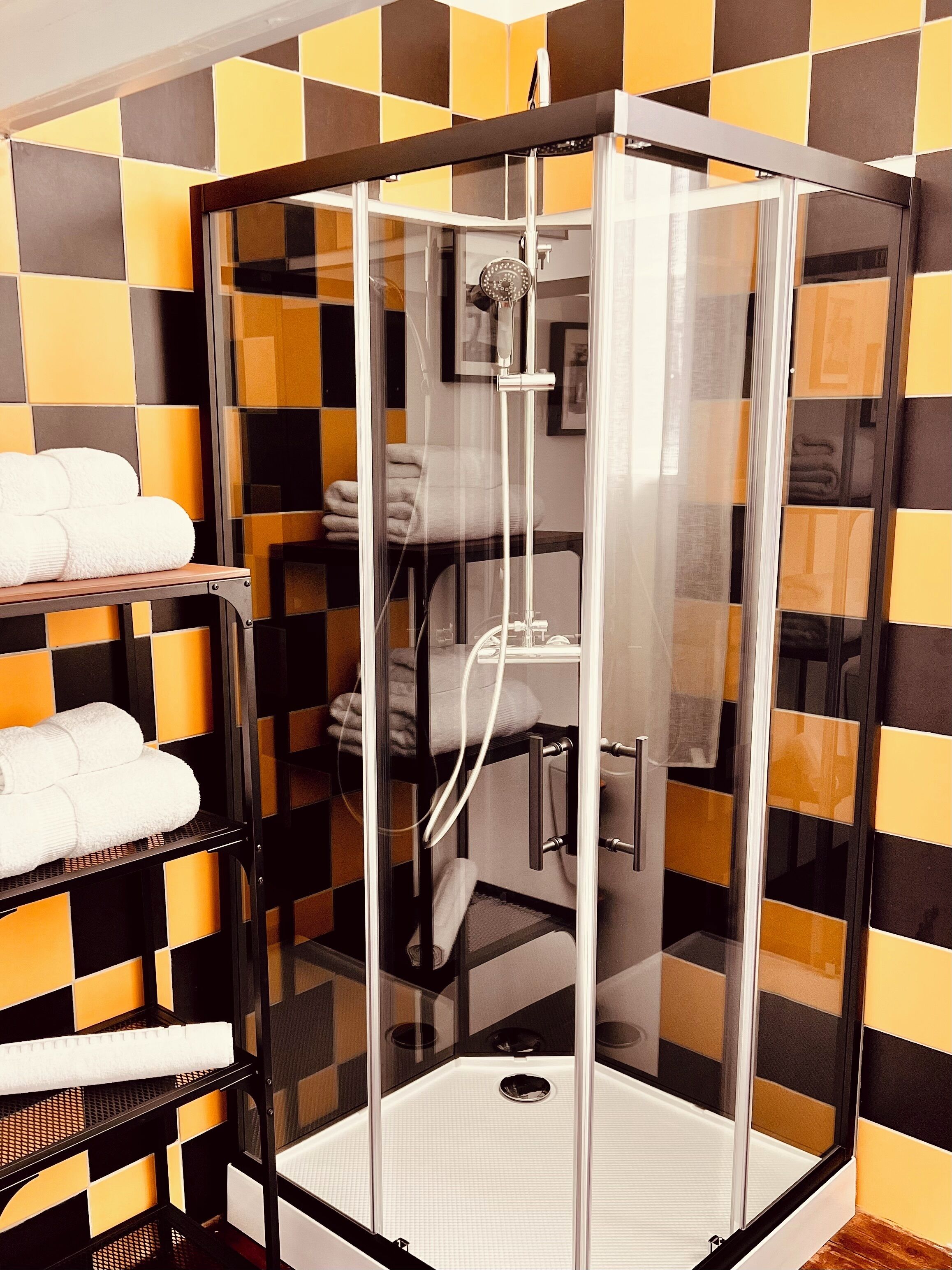 A glass-enclosed shower stall with a white tiled floor and a towel rack with folded towels.