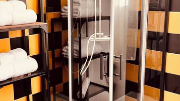 A glass-enclosed shower stall with a white tiled floor and a towel rack with folded towels.