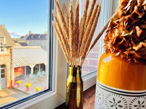 A window with a vase of dried wheat stalks and a decorative container with a patterned design. - La Récréation (Chatelaudren)
