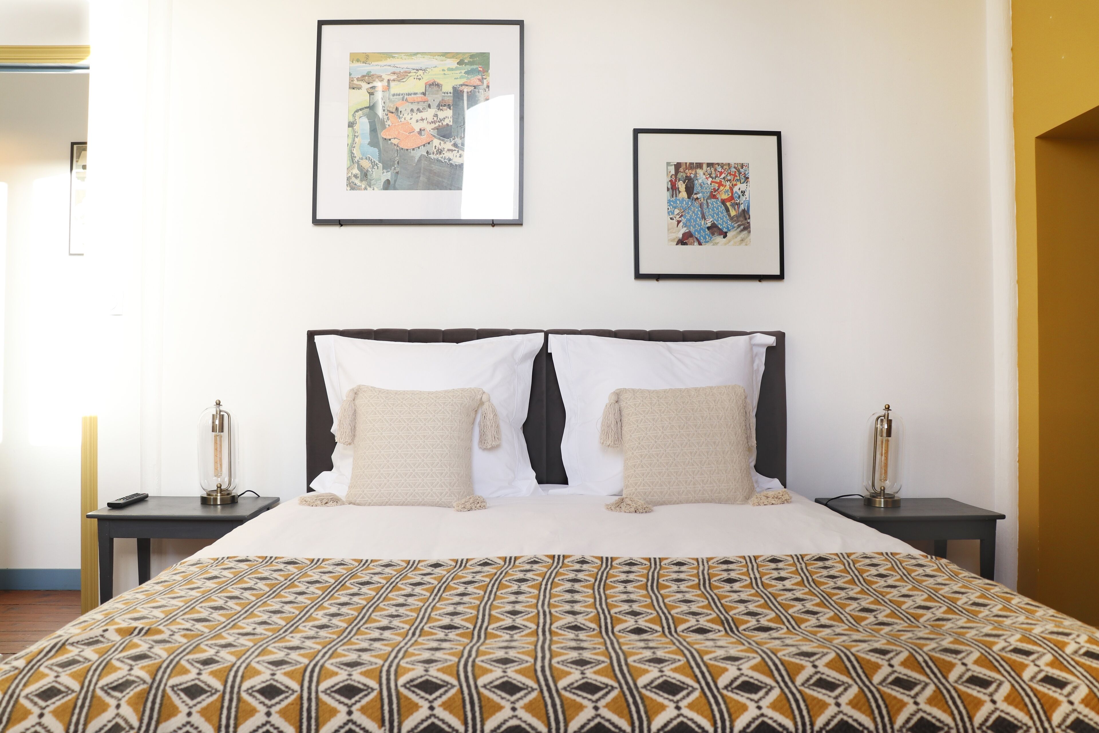 A neatly made bed with patterned bedding, two bedside tables with lamps, and two framed artworks on the wall.