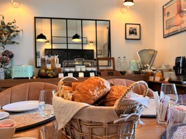 Uma área de refeições com uma cesta de pão, uma máquina de café e uma mesa posta para o café da manhã.