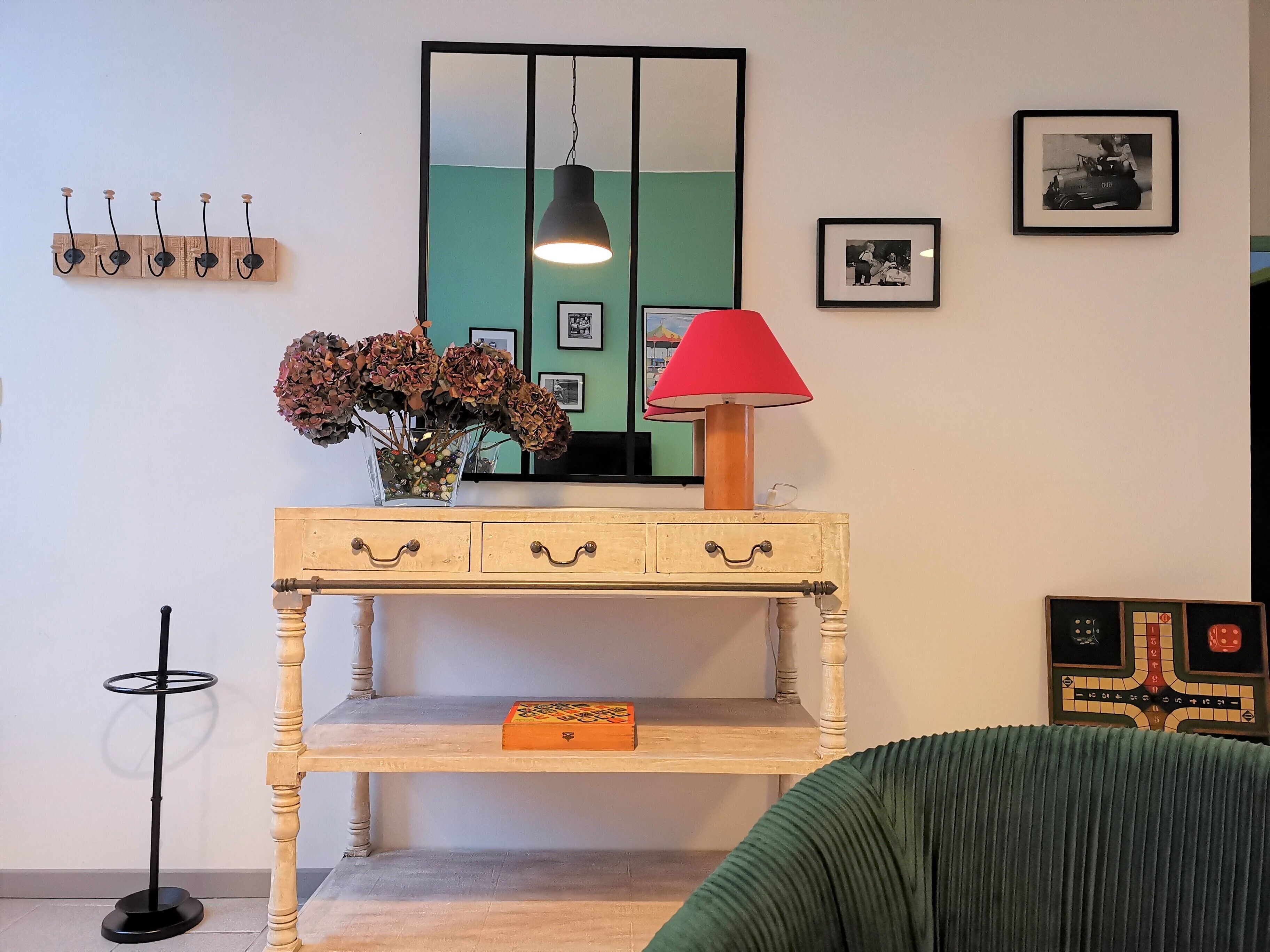 A room with a wooden console table, a mirror, a red lamp, and a chessboard.