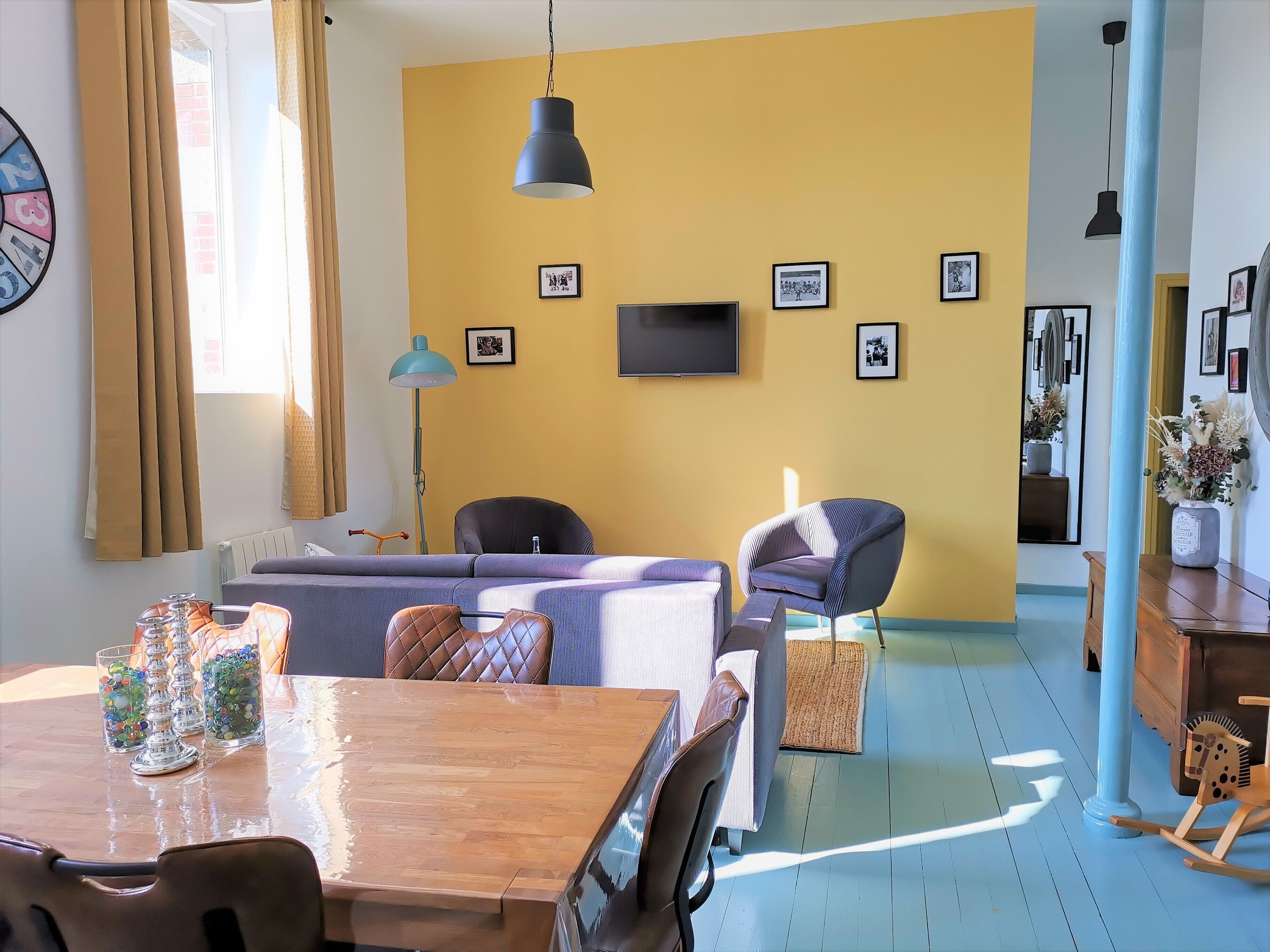 A modern living room with a sofa, chairs, a wooden dining table, and a TV mounted on the wall.