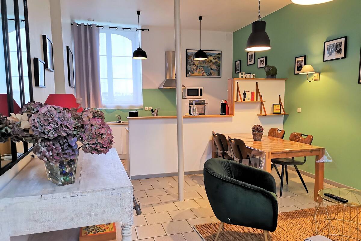 A modern living room with a dining area, featuring a white table, a black chair, and a green wall.
