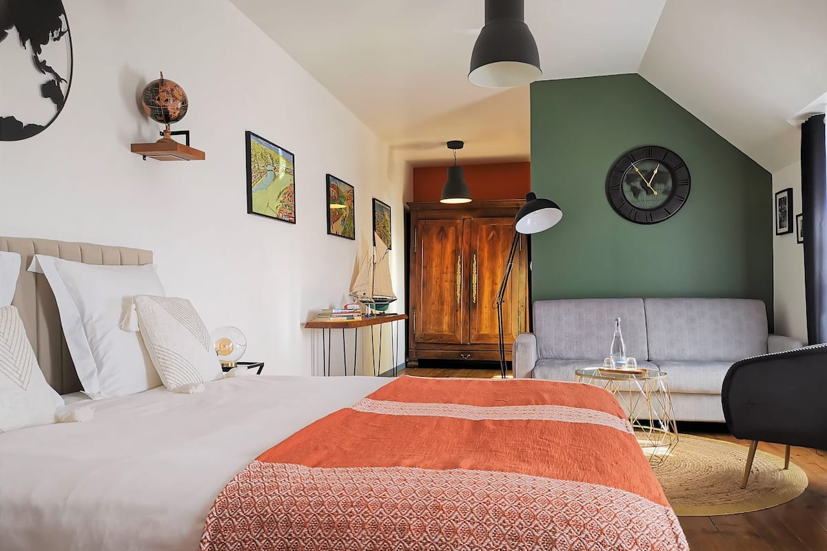 A bedroom with a large bed, a desk with a globe, a clock, and a green wall.