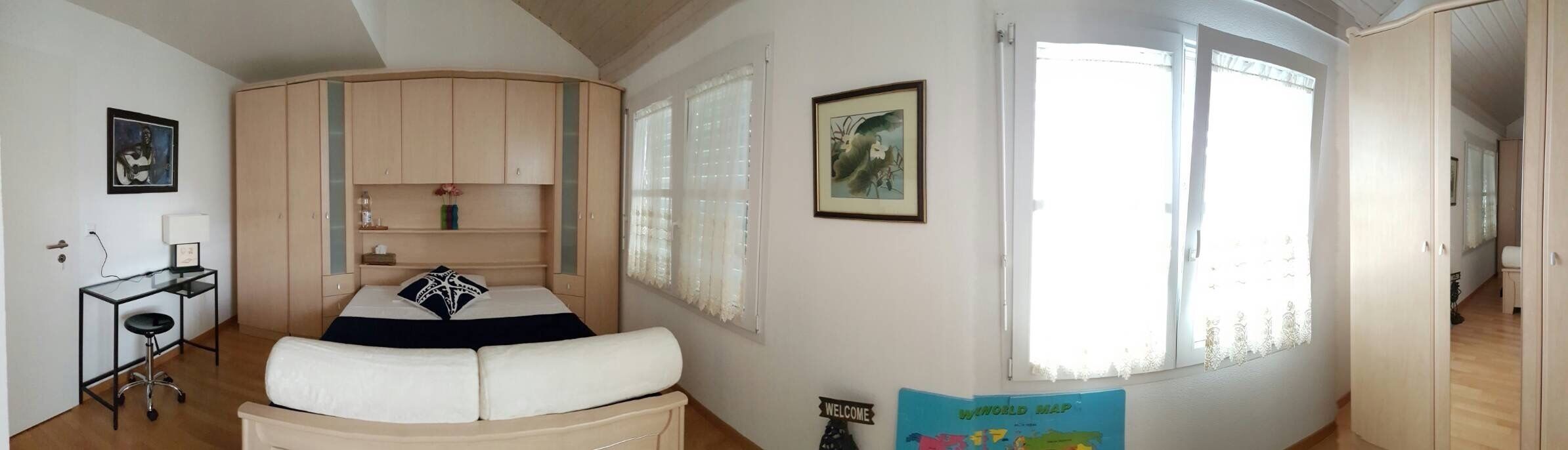 A bedroom with a bed, a desk, a chair, a wardrobe, and a window with curtains.