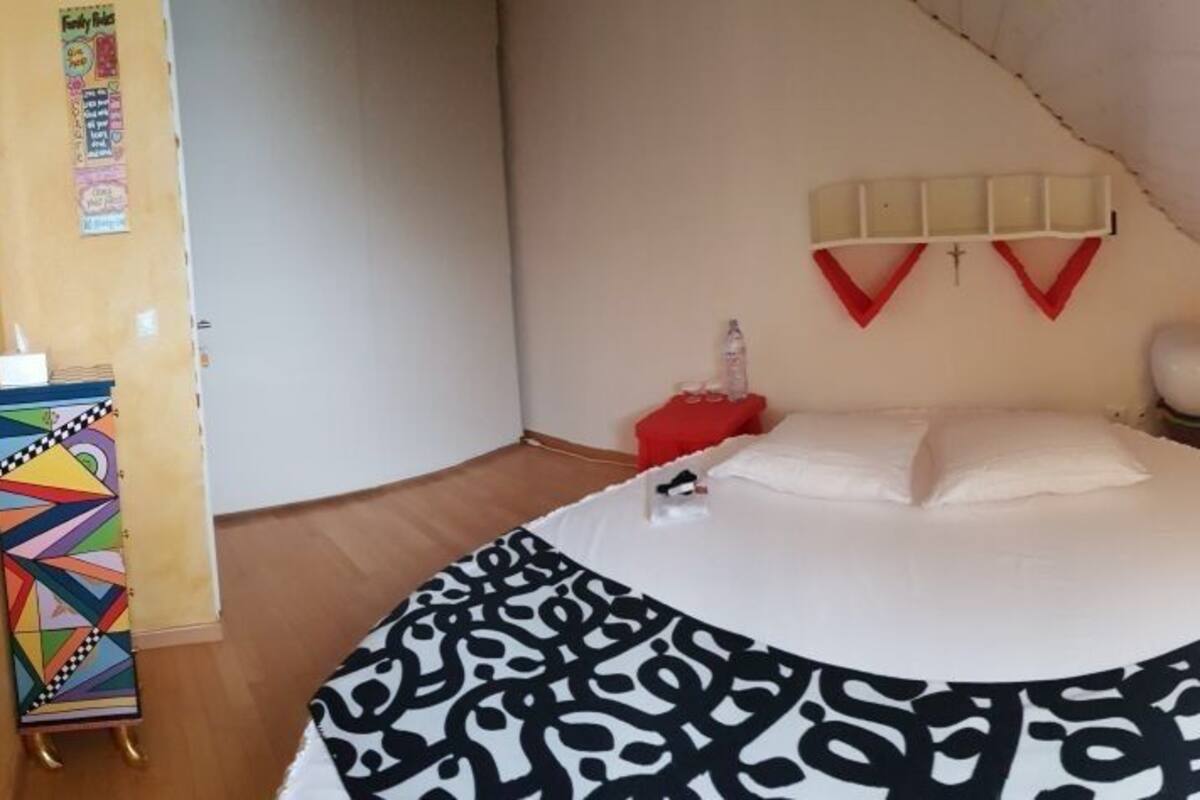 A bedroom with a bed, a red nightstand, a white wall decoration, and a window.