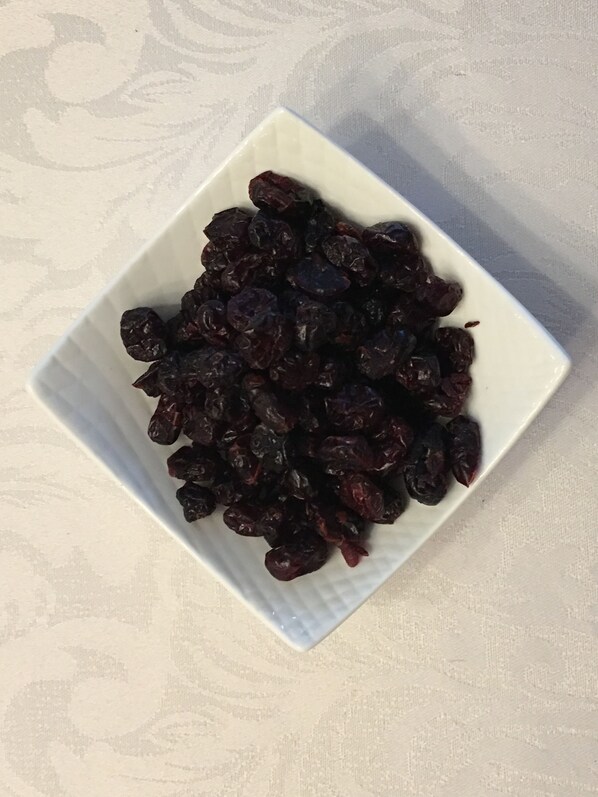A white square plate filled with dark-colored dried fruits, placed on a textured surface.