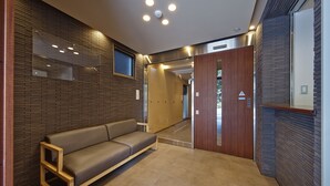 A modern lobby with a wooden bench, a reception desk, and a door leading to another area. - No6 Nijo (Kyoto)