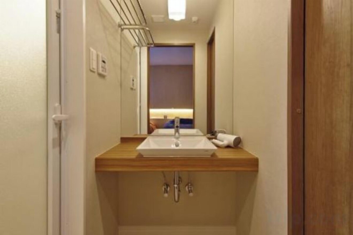 A narrow hallway leading to a bathroom with a wooden vanity, a mirror, and a sink.