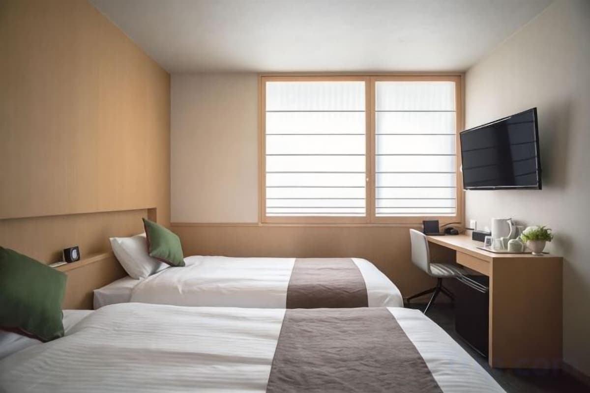 Una habitación de hotel con dos camas, un escritorio, una silla, un televisor y una ventana.
