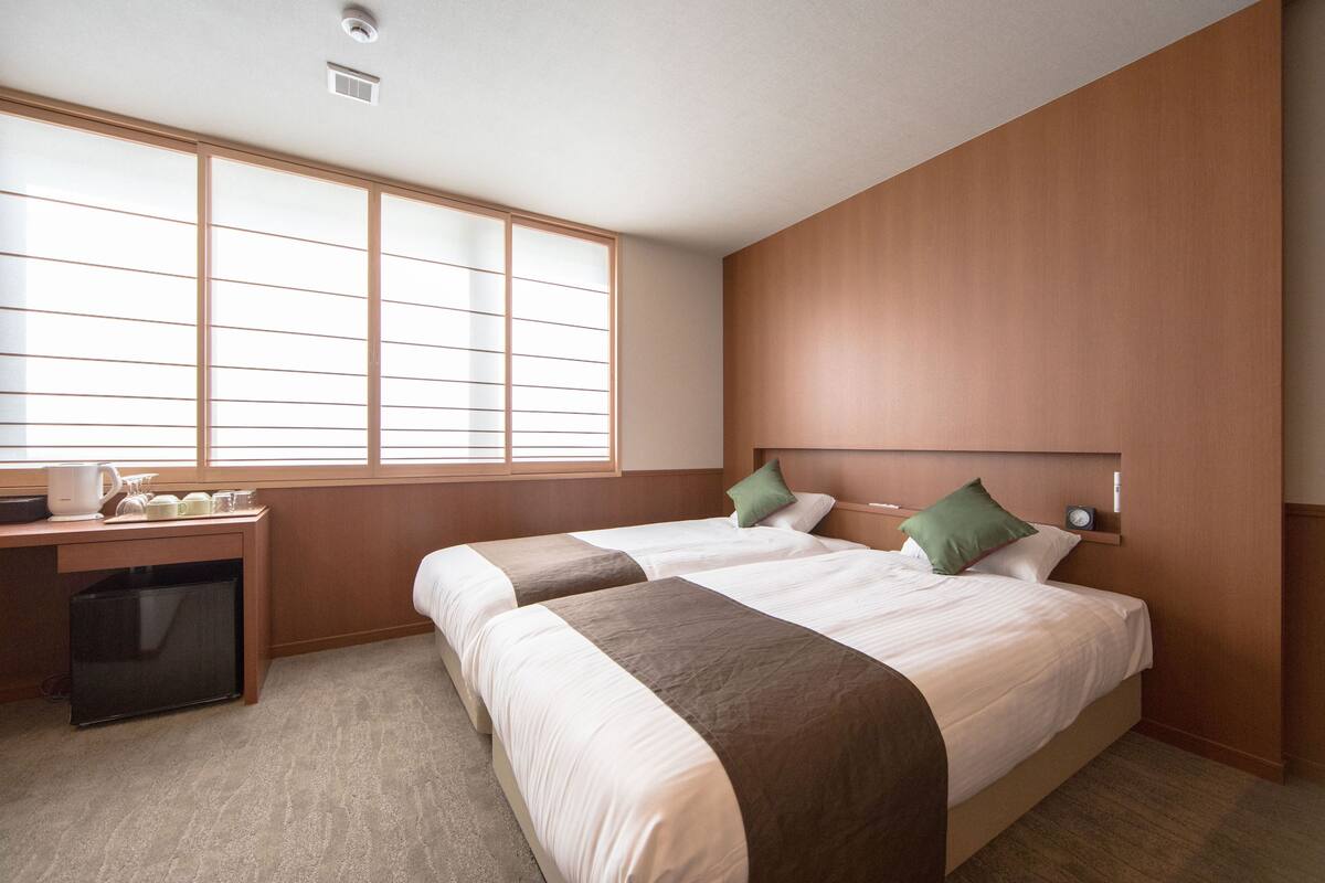A hotel room with two beds, a desk, and a window.