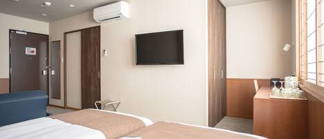Habitación de hotel con dos camas, televisión, escritorio con cafetera y ventana con persianas.