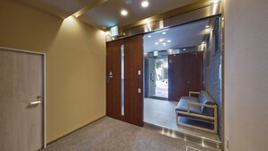 A hallway with a wooden door, a bench, and a glass door leading to a seating area. - No6 Nijo (Kyoto)