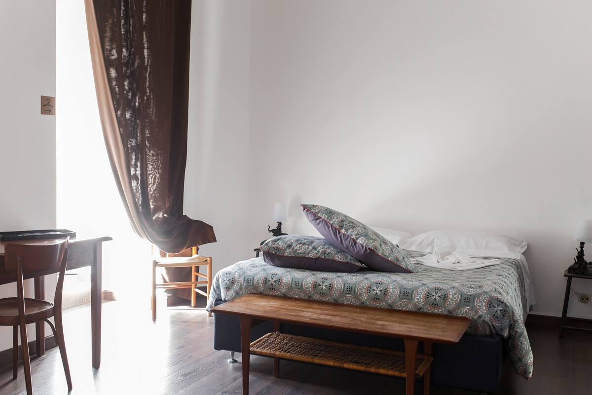 A bedroom with a bed, a wooden bench, a desk, and a chair.