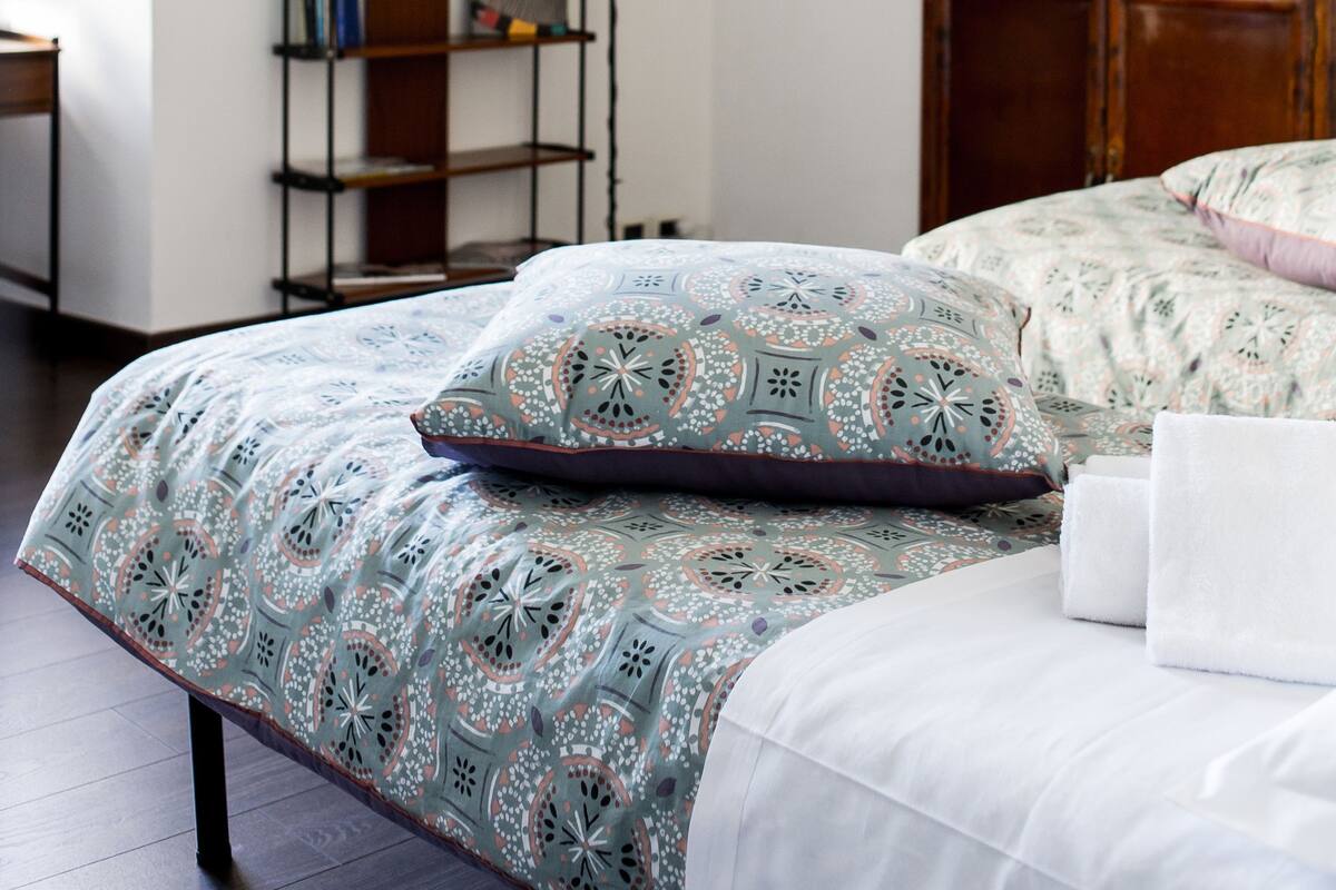 A bedroom with a bed, a wooden wardrobe, a wall-mounted shelf, and a decorative wall piece.