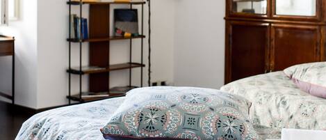 A bedroom with a bed, a wooden wardrobe, a wall-mounted shelf, and a decorative wall piece.