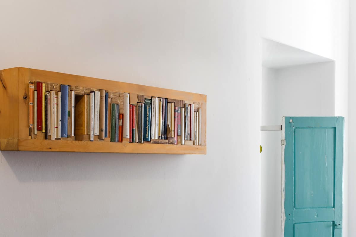 A room with a wooden bookshelf against the wall, a teal door, and a patterned bedspread.