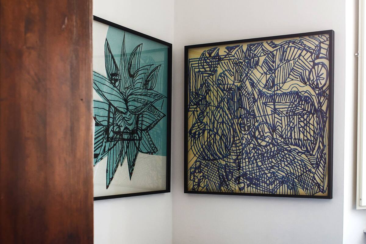 A bedroom with a bed, a wooden wardrobe, and two framed abstract artworks on the wall.