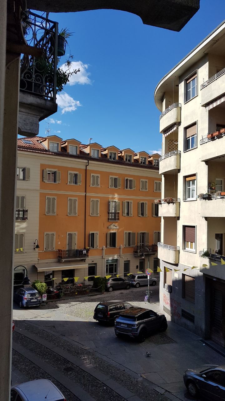 Une vue de rue avec des immeubles à plusieurs étages, des balcons et des voitures garées.