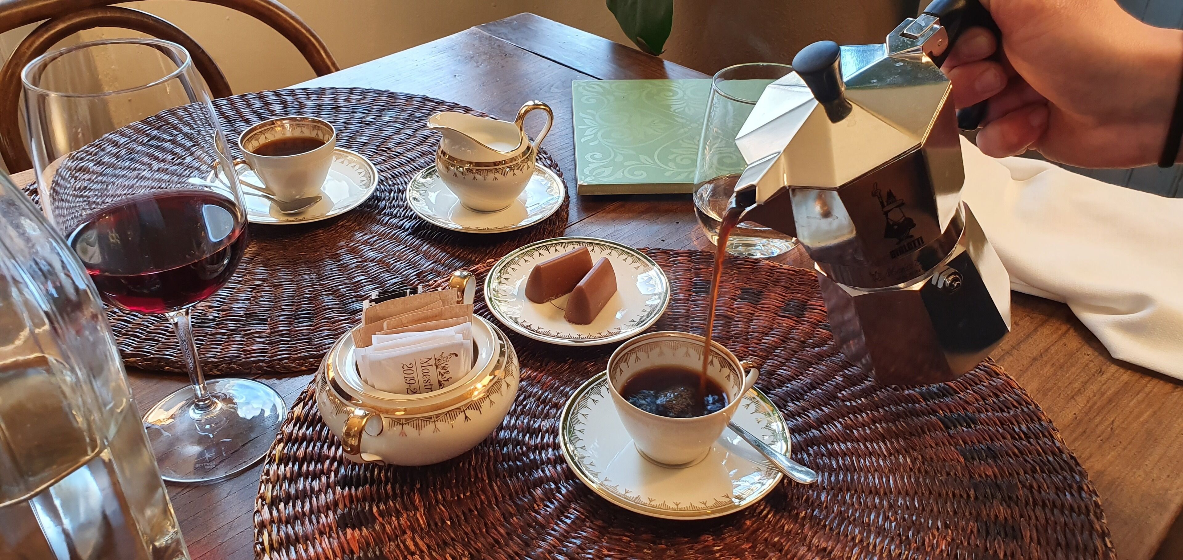 A table set with various cups of coffee and tea, a glass of red wine, and a decorative jug.