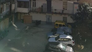 Um edifício residencial de vários andares com varandas, uma área de estacionamento com carros e céu claro.