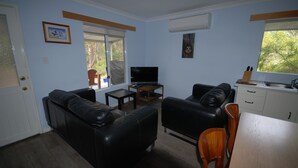 Uma sala de estar com sofá, televisão, mesinha e um espaço de refeições com mesa e cadeiras de madeira.