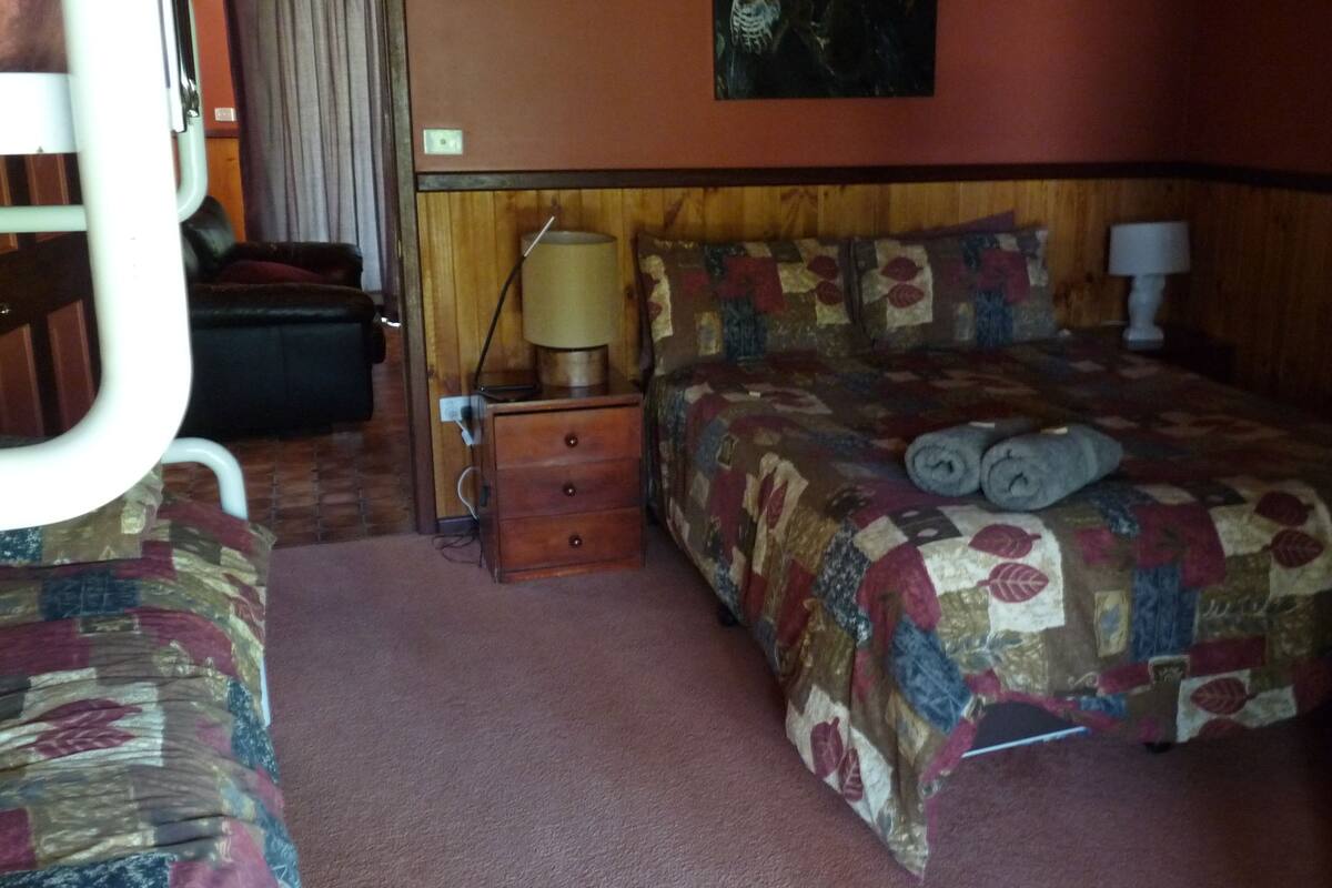 A hotel room with a bed, a nightstand, a lamp, and a suitcase.
