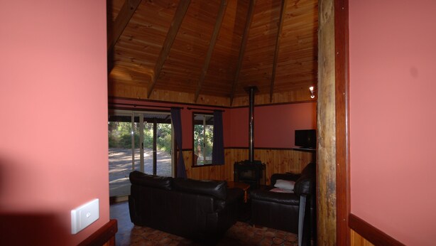 Interior acolhedor de uma cabana com teto de madeira, lareira e sofá de couro.