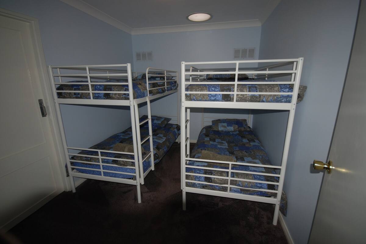A room with three bunk beds against a wall, a door, and a ceiling light.
