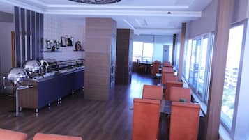 A modern restaurant with a long counter, orange chairs, and large windows.