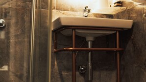 Un baño con cabina de ducha de vidrio, un lavamanos con base de cobre y un espejo con marco circular.