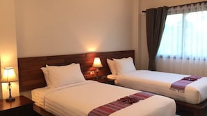Quarto de hotel com duas camas de solteiro, cabeceiras de madeira, abajures e uma janela com cortinas.