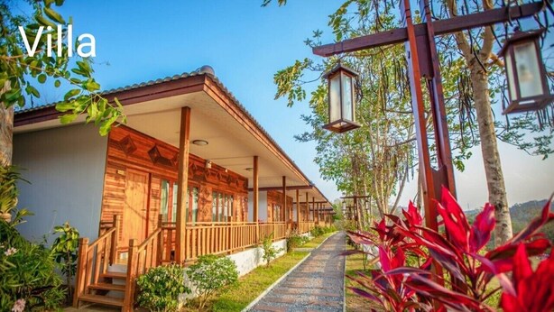 Uma villa com fachada de madeira, varanda coberta e caminho de cascalho que leva à entrada.