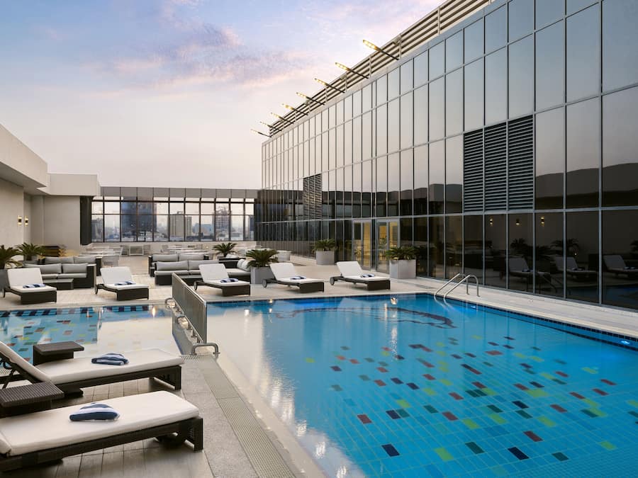 A rooftop pool with lounge chairs and a glass building in the background.