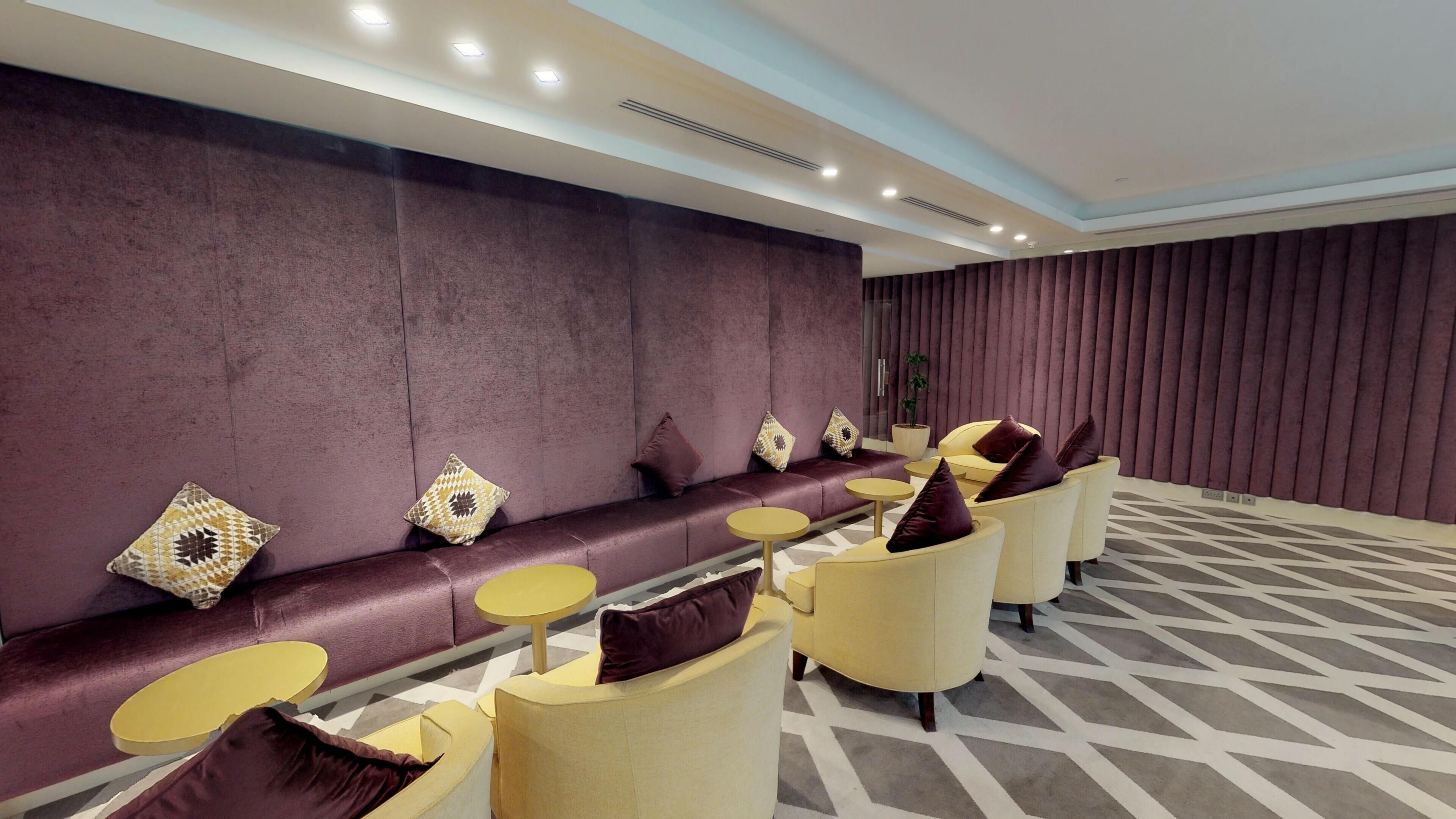 A modern lounge with a sofa, chairs, and small tables, featuring a patterned floor and a wall with vertical panels.