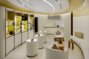 Interior moderno de una cafetería con área de asientos, una barra con opciones de café y una pared mostrando diferentes tipos de café.