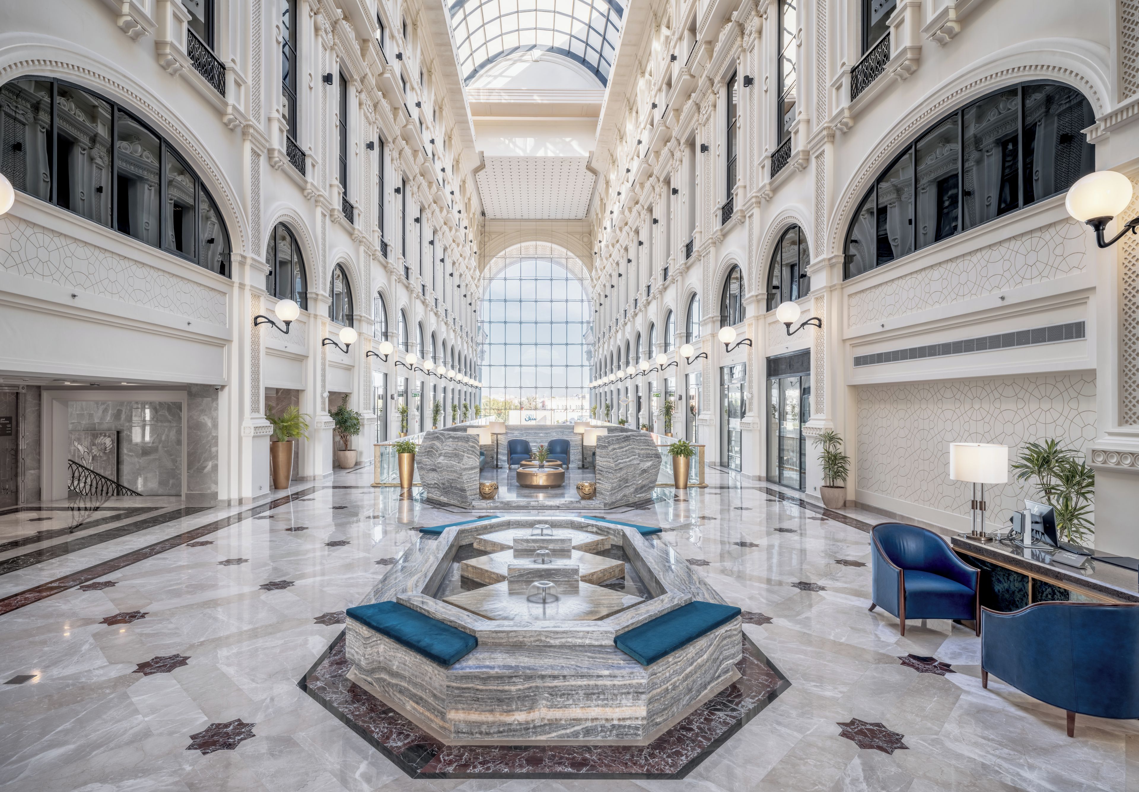 Un hall d’entrée spacieux, doté d’une fontaine centrale, d’un sol en marbre et d’un plafond haut avec des puits de lumière.