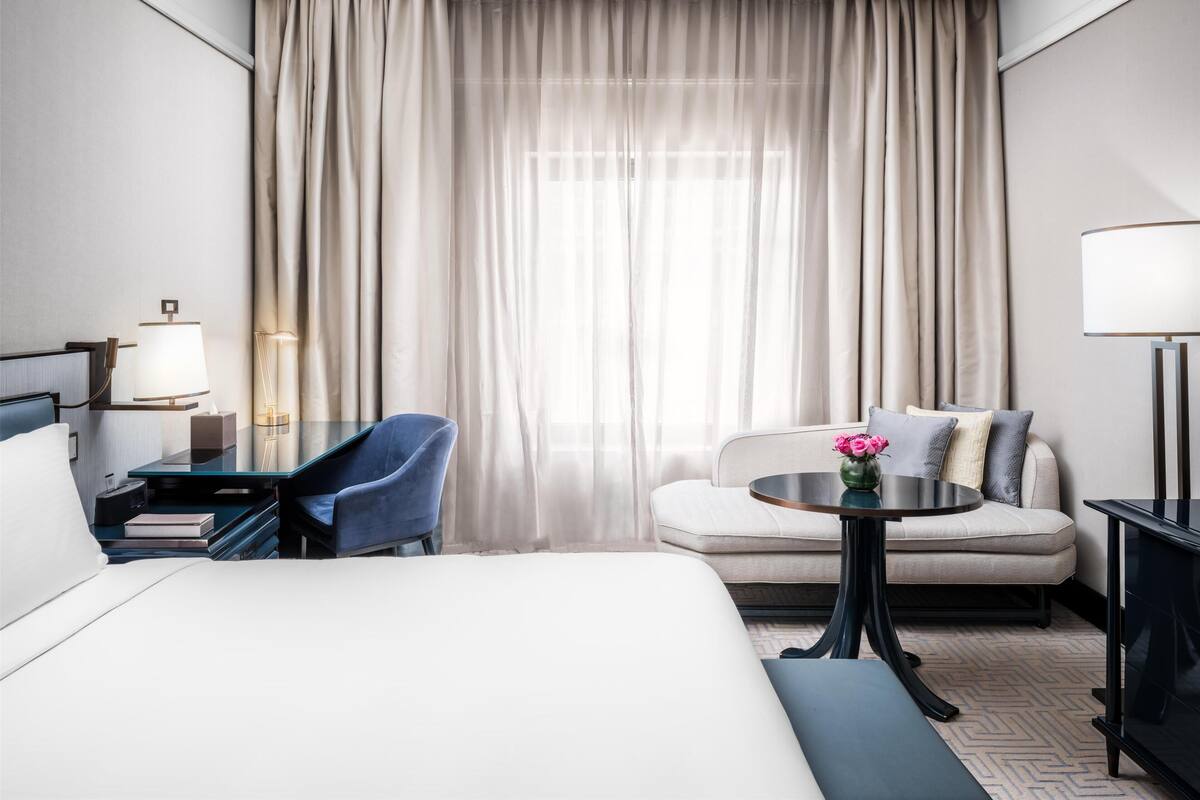 Een hotelkamer met een bed, een bureau met een lamp, een stoel, een bank en een kleine tafel met een bloevas.