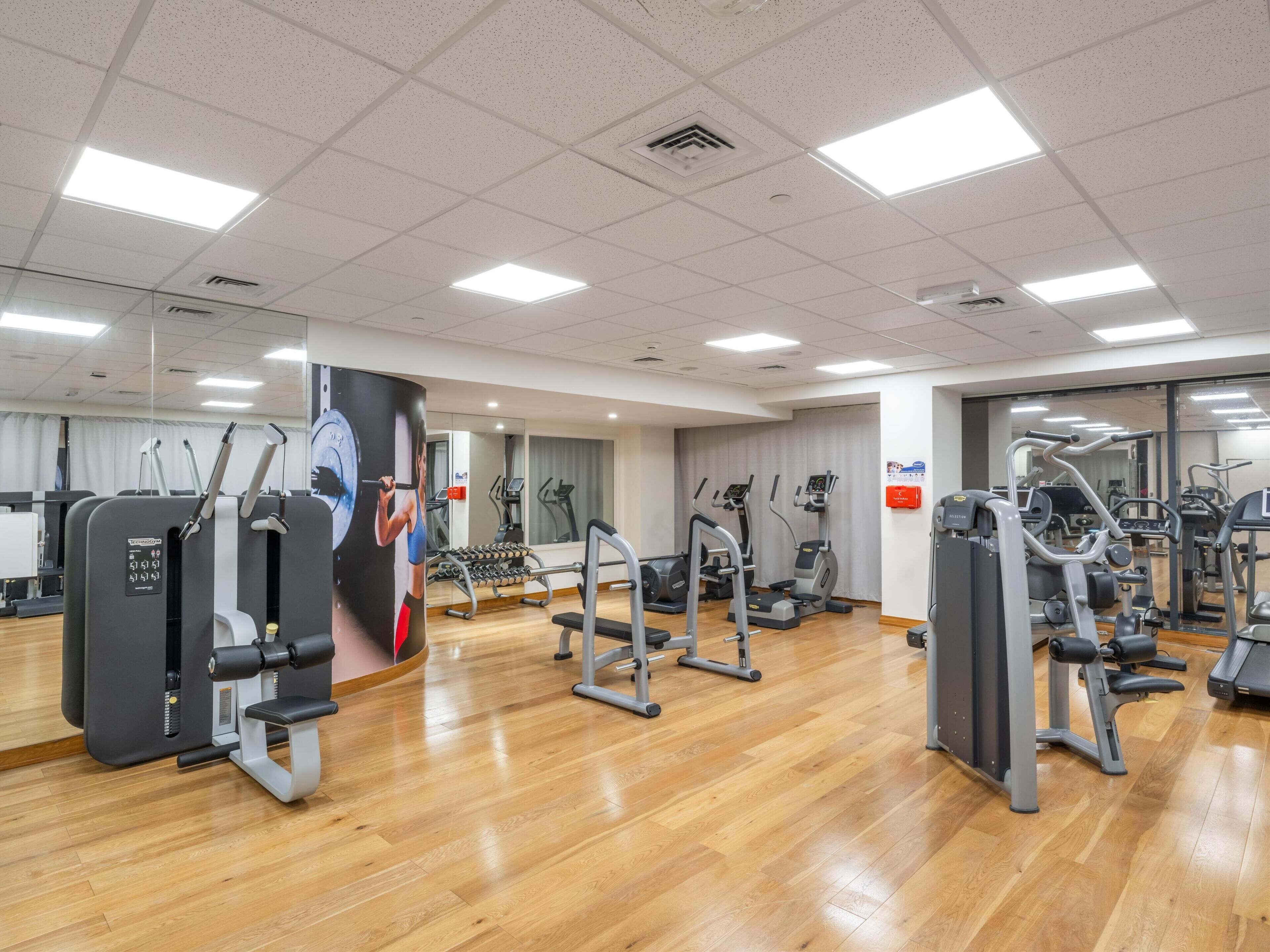 Un gimnasio con diferentes máquinas de ejercicio, suelo de madera y un espejo grande.