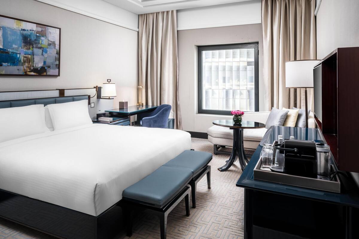Een hotelkamer met een groot bed, een bureau met lamp, een stoel, een ronde tafel met vaas, en een televisie.